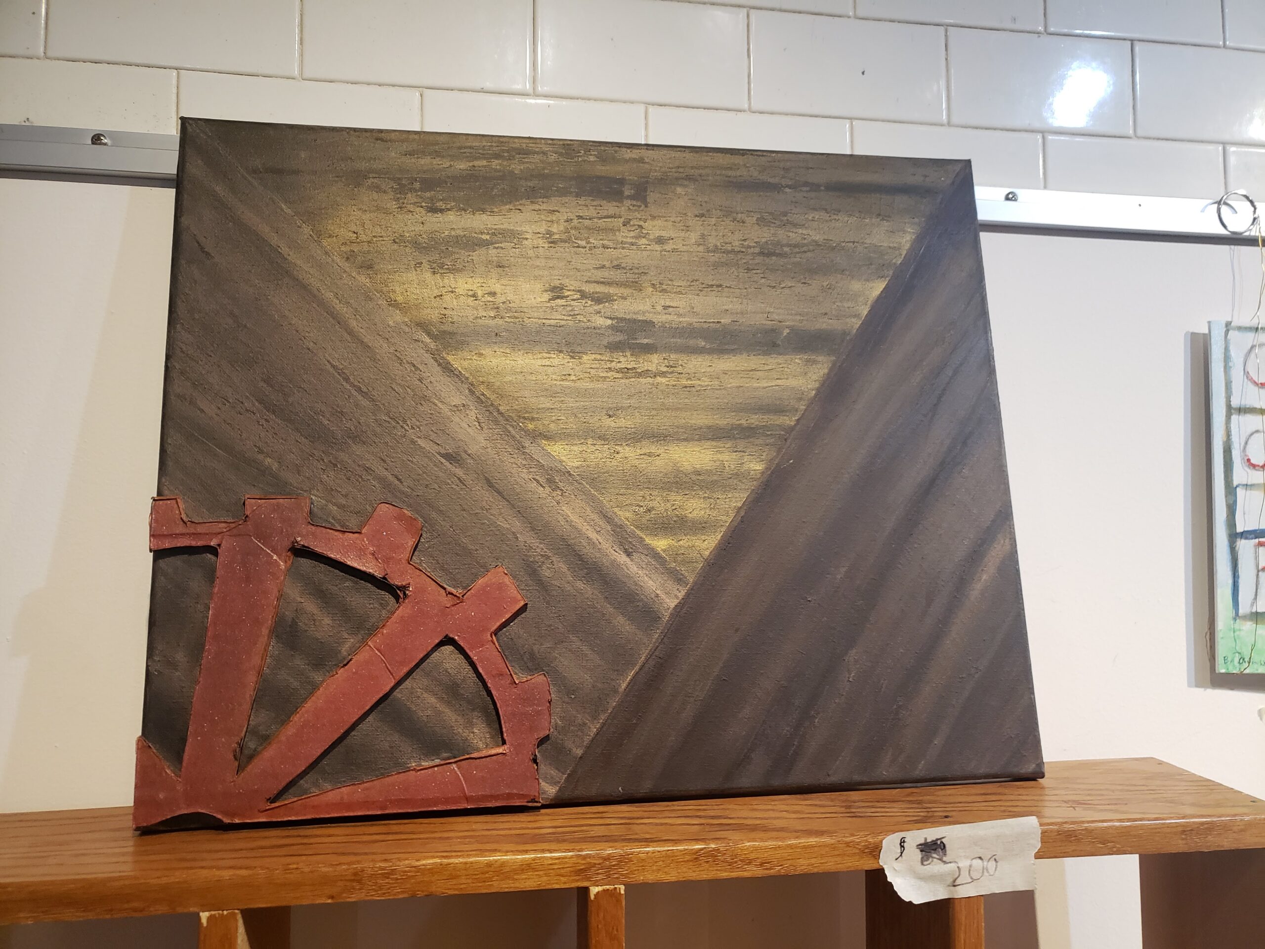 A photo o f a painting showing gradiating stripes and a rust colored cog on the painting on the lower left hand side on top of a wooden shelf.