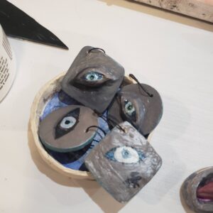 four evil eyes, two more 3D and two more flat, all on gray backgrounds and with metal hookshaped pins.