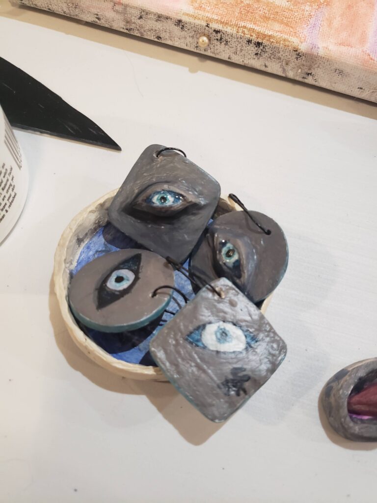 four evil eyes, two more 3D and two more flat, all on gray backgrounds and with metal hookshaped pins.