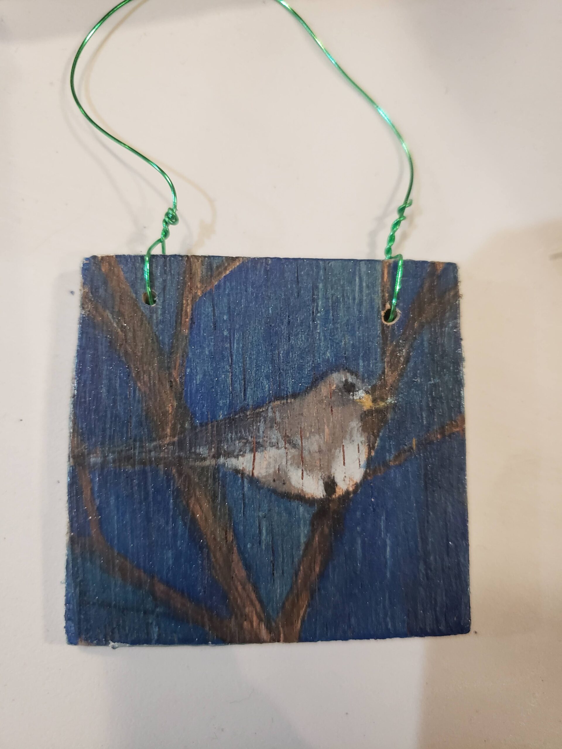 A watercolor painting of a Dark Eyed Junco on a tree branch with a dark blue background, painted on plywood.