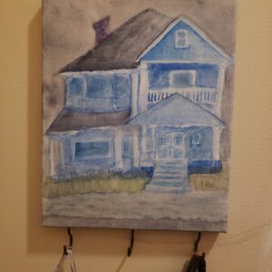 a watercolour on canvas of a brooding, slightly distorted, blue Victorian home floating on a gray lake with gray skies. there are three hooks on teh bottom of the canvas in a tarnished brass kind of colour that can hold keys or other items