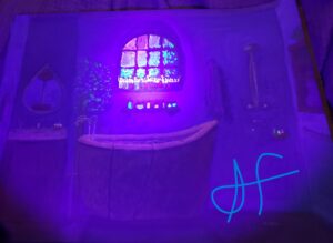 same image but bathed in purple light which makes some things like the window, candles, soap bottles, and leaves glow