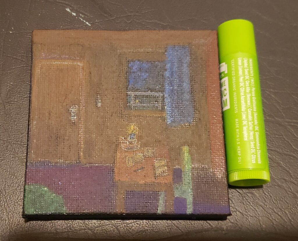 a small canvas only slightly taller than a tube of chapstick, depicts the inside of a treehouse with a table, chair, rug, door, window, curtains. there's a candle, papers, writing instrument, and book on the table, a key hangs on the wall. out side the window is a railing and darkening bit of sky