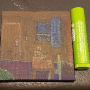 a small canvas only slightly taller than a tube of chapstick, depicts the inside of a treehouse with a table, chair, rug, door, window, curtains. there's a candle, papers, writing instrument, and book on the table, a key hangs on the wall. out side the window is a railing and darkening bit of sky
